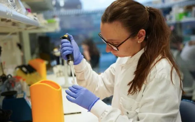 Una mujer introduce una jeringa en un recipiente en un laboratorio.